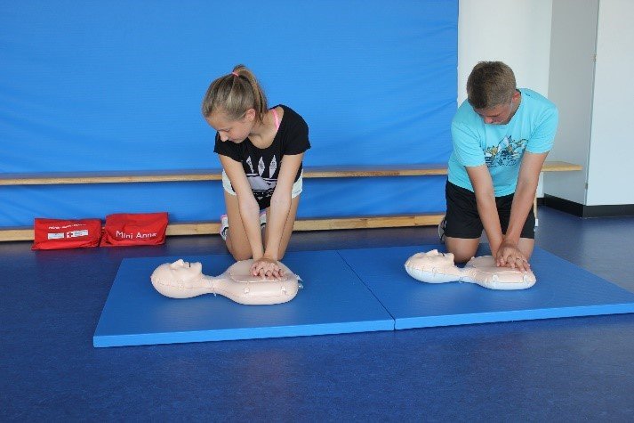 Ein Junge und ein Mädchen üben an einer Übungspuppe die Herz-Lungen-Wiederbelebung